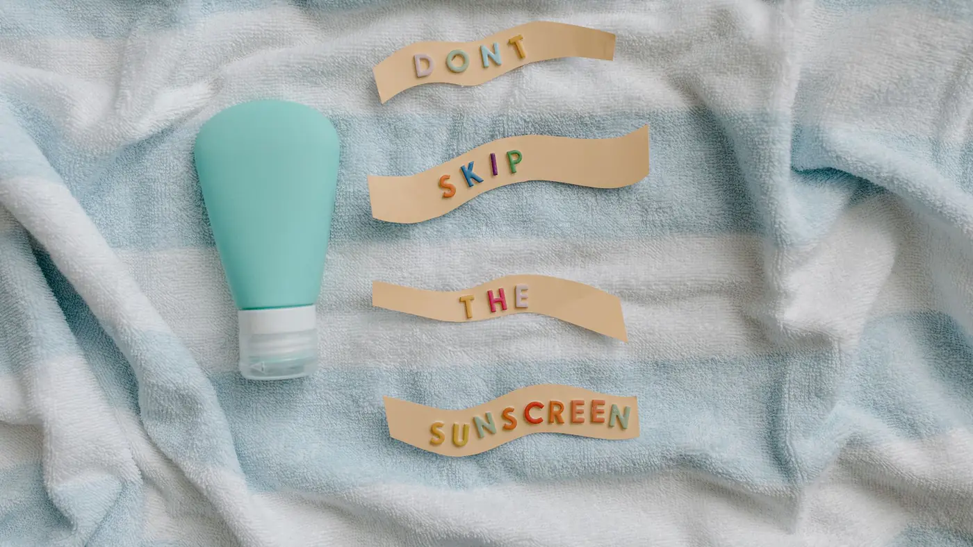 Flat lay of sunscreen bottle with message 'Don't skip the sunscreen' on a towel.