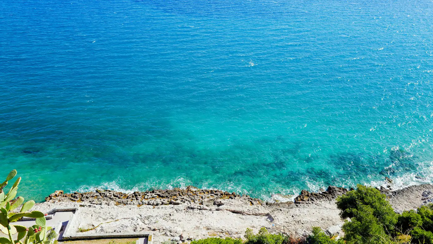 A breathtaking aerial view of vibrant blue ocean and rocky shoreline on a sunny day.