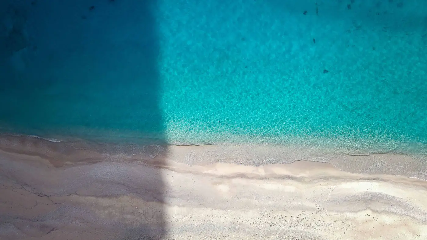 Stunning aerial shot of a sandy beach meeting vibrant turquoise waters, ideal for summer travel imagery.