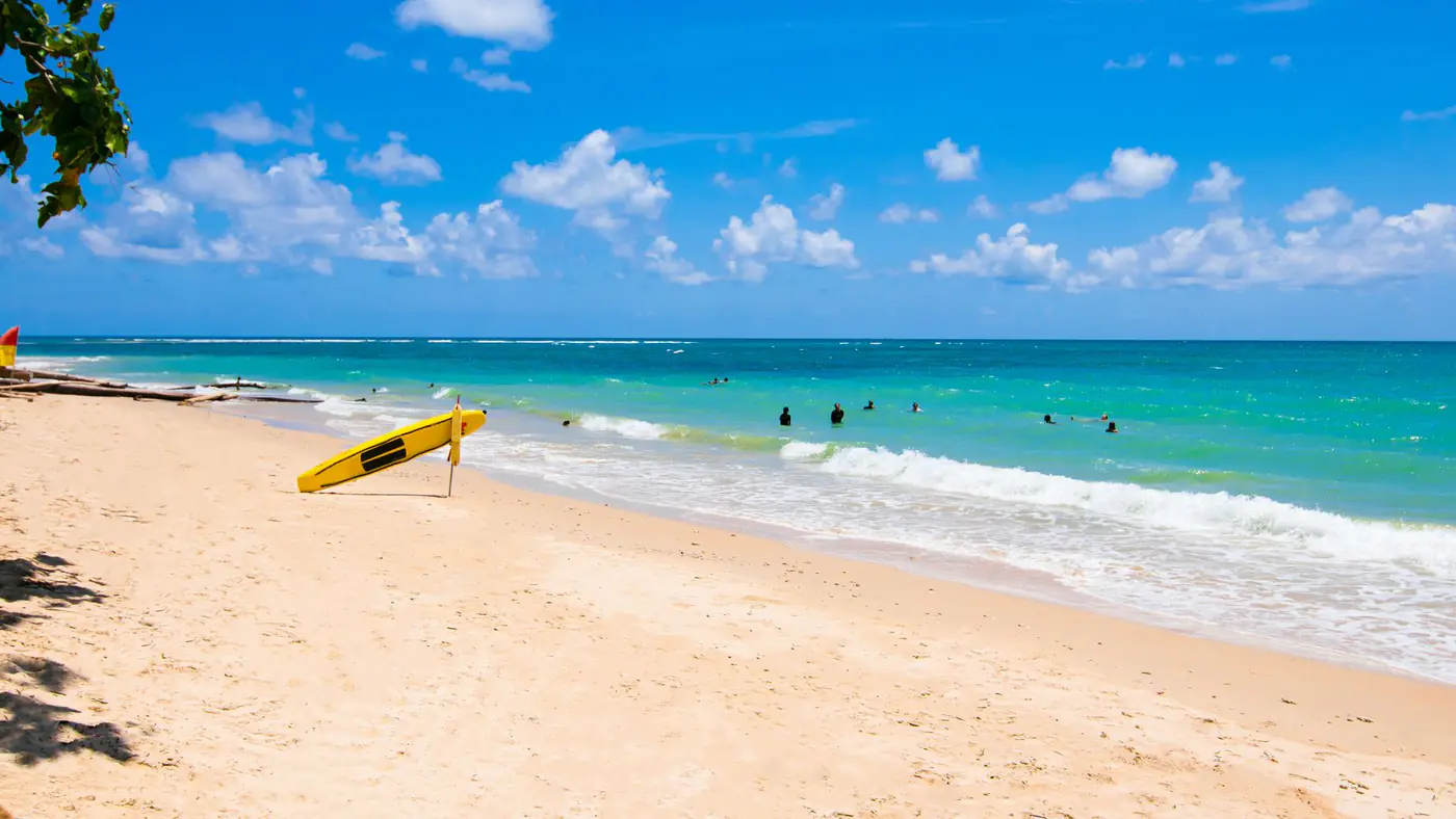 Idyllic tropical beach with turquoise waters, sandy shore, and a yellow surfboard under a bright blue sky.