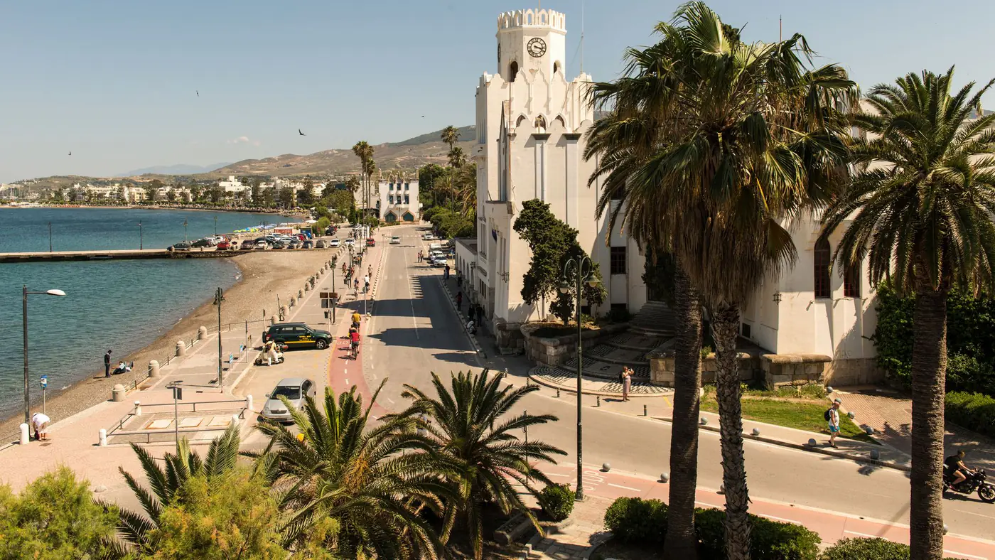 Charming street view of Kos, Greece with palm trees and historic architecture under a bright summer sky.