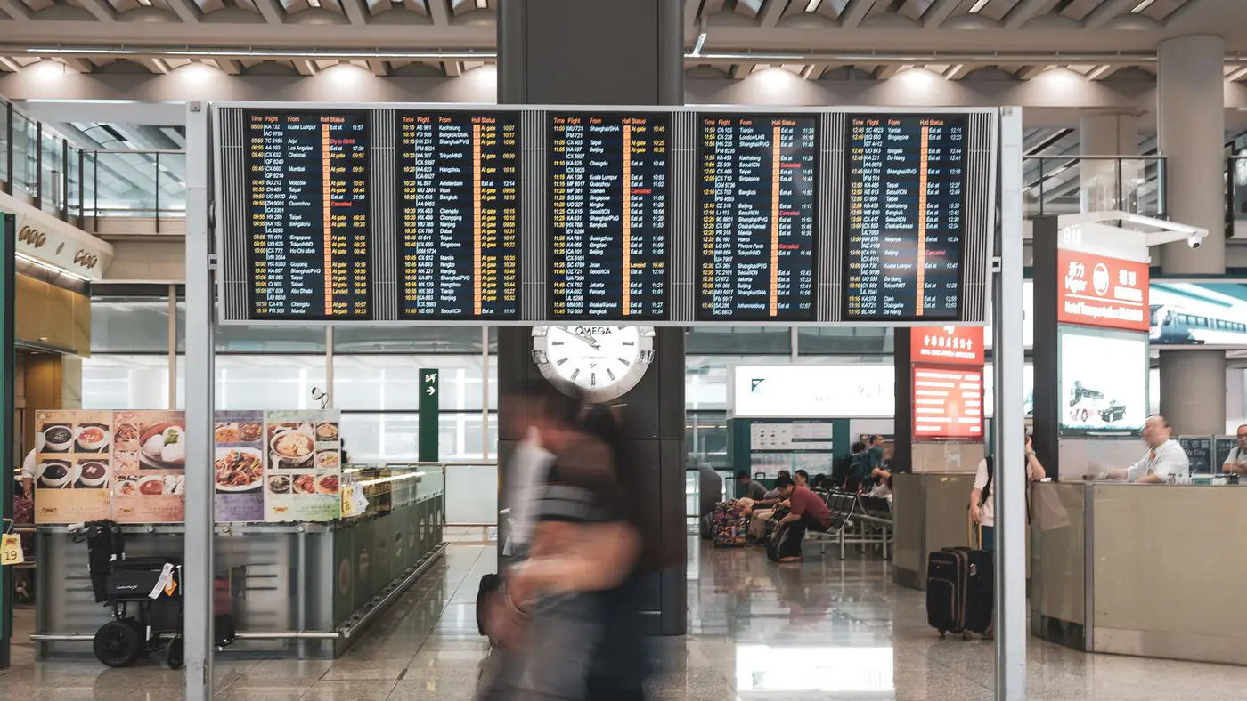 Blurred motion of travelers in a modern airport terminal with departure screens and a prominent clock.