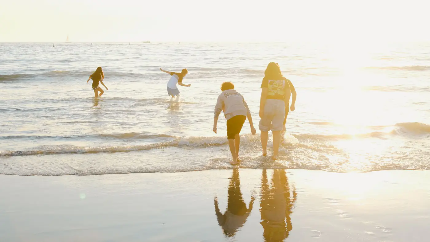 People playing in the gentle waves of a sunlit beach, captured during daytime.