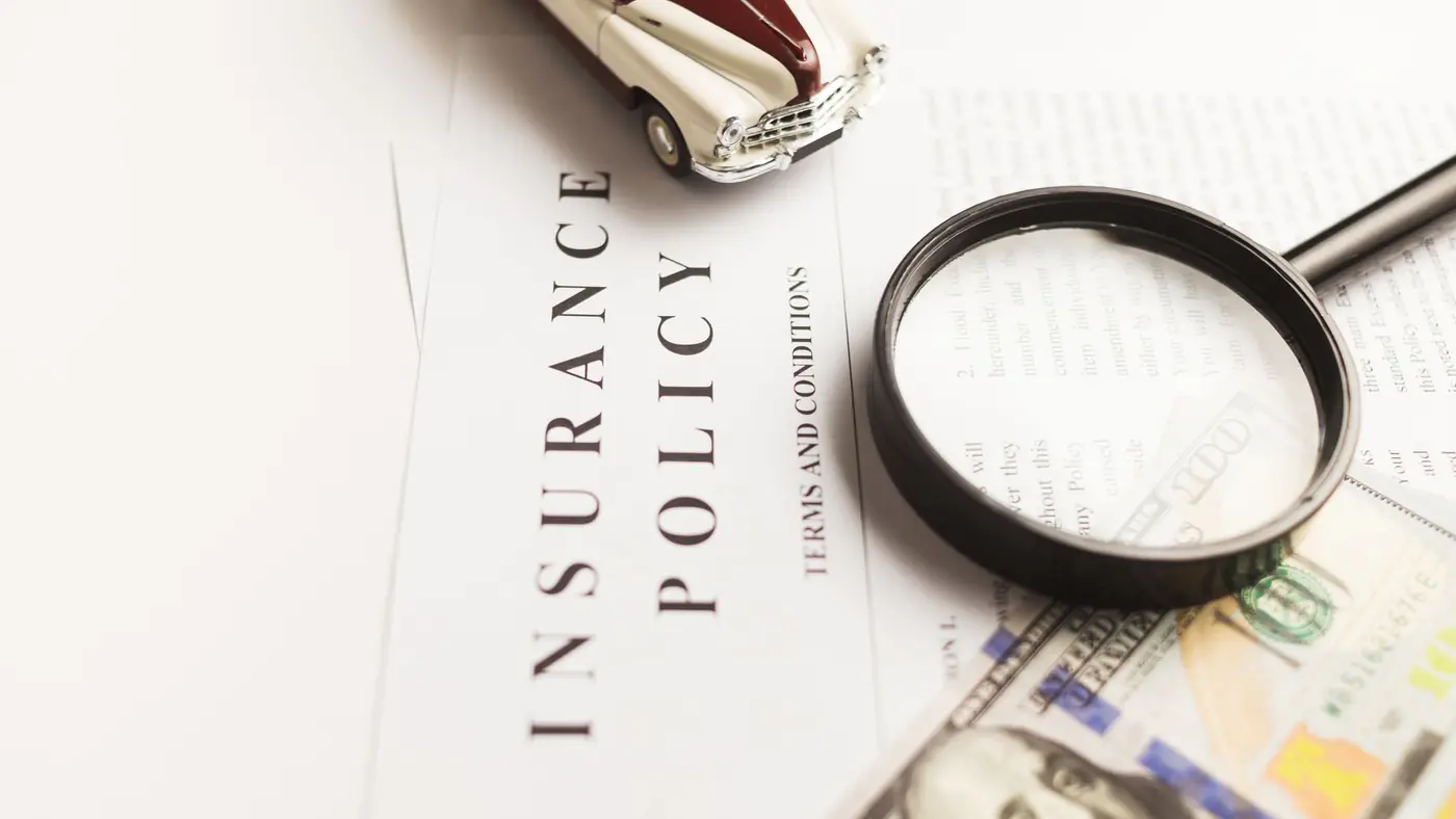 Close-up image of an insurance policy with a magnifying glass, money, and toy car.
