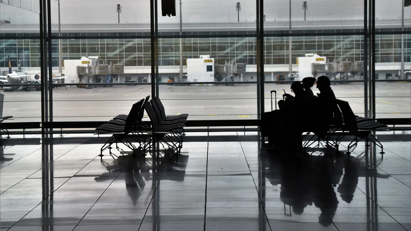 Silhouette of unrecognizable passengers sitting on chairs with luggage near  window and waiting for flight