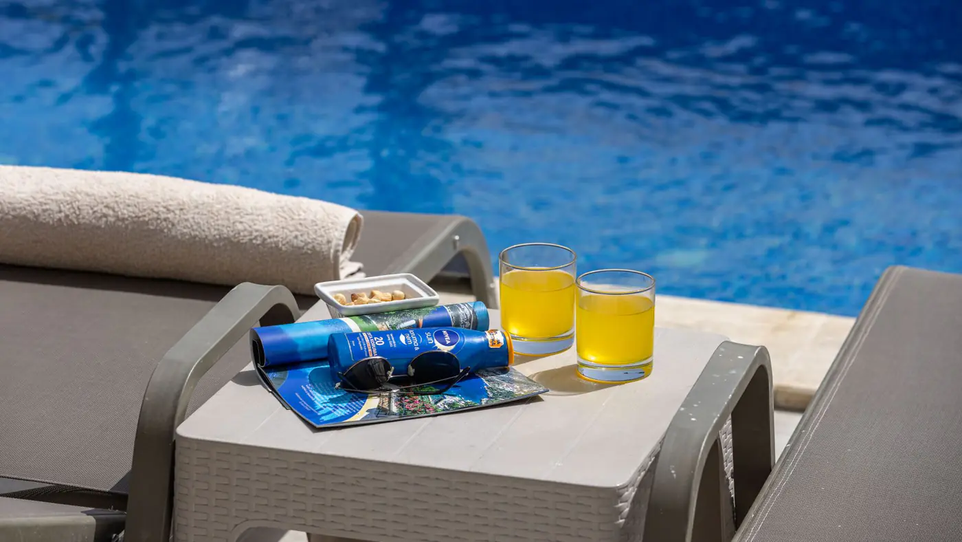 A sunlit poolside setup in Antalya, Türkiye, featuring drinks and sunscreen.