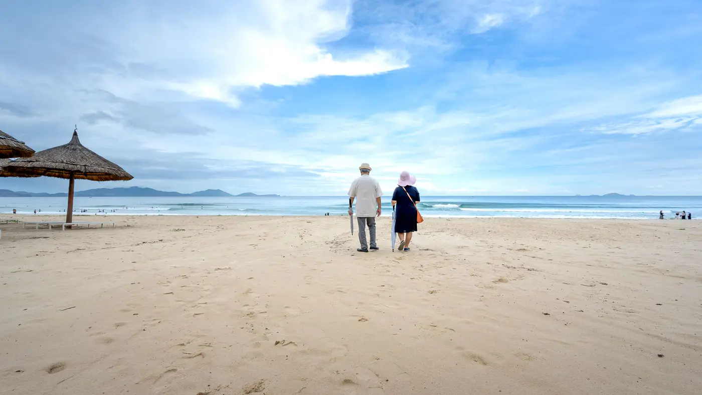 Senior couple enjoying a peaceful walk on a sandy beach under a wide blue sky.