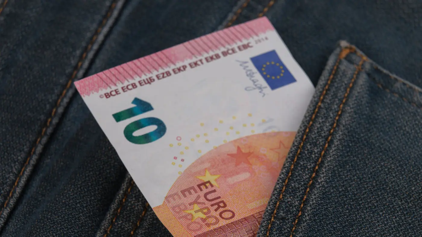 Close-up of a 10 euro banknote sticking out from a denim pocket.