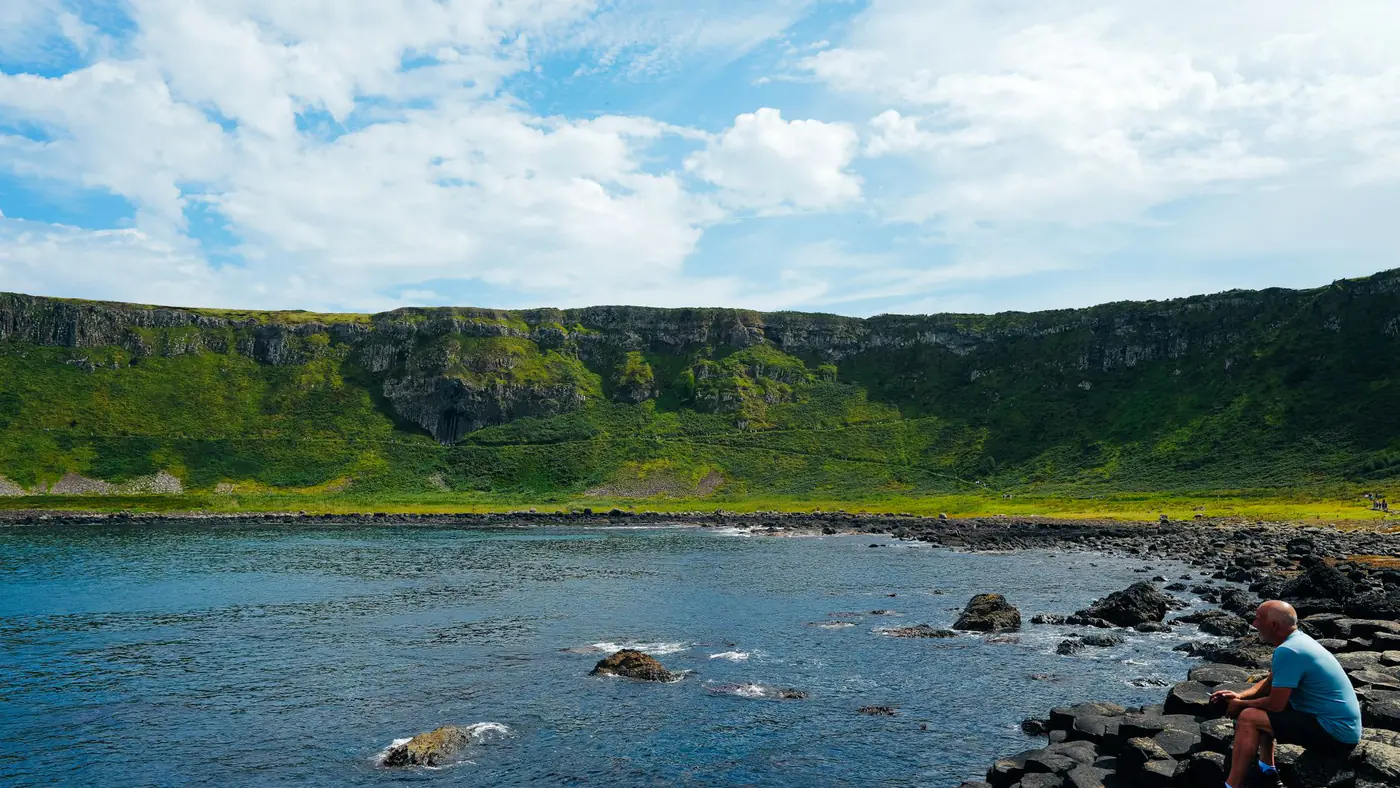 A man sits on the rocky coast of Giant's Causeway, enjoying the scenic view.