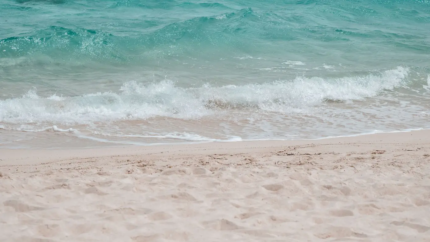A serene beach scene with gentle turquoise waves lapping against clean sandy shores on a sunny day.