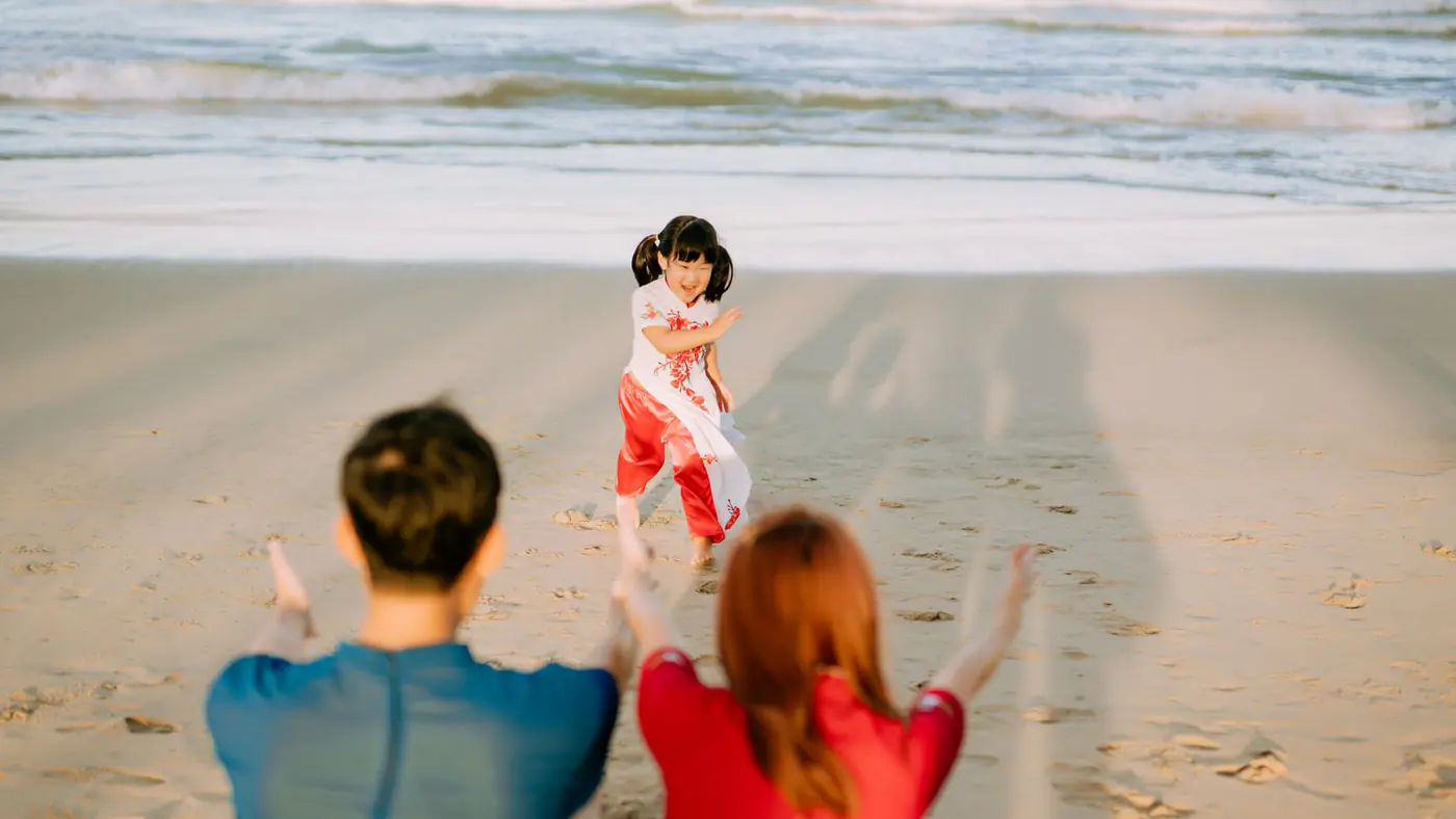 Joyful family moment with child running to parents on a sandy beach during sunset.