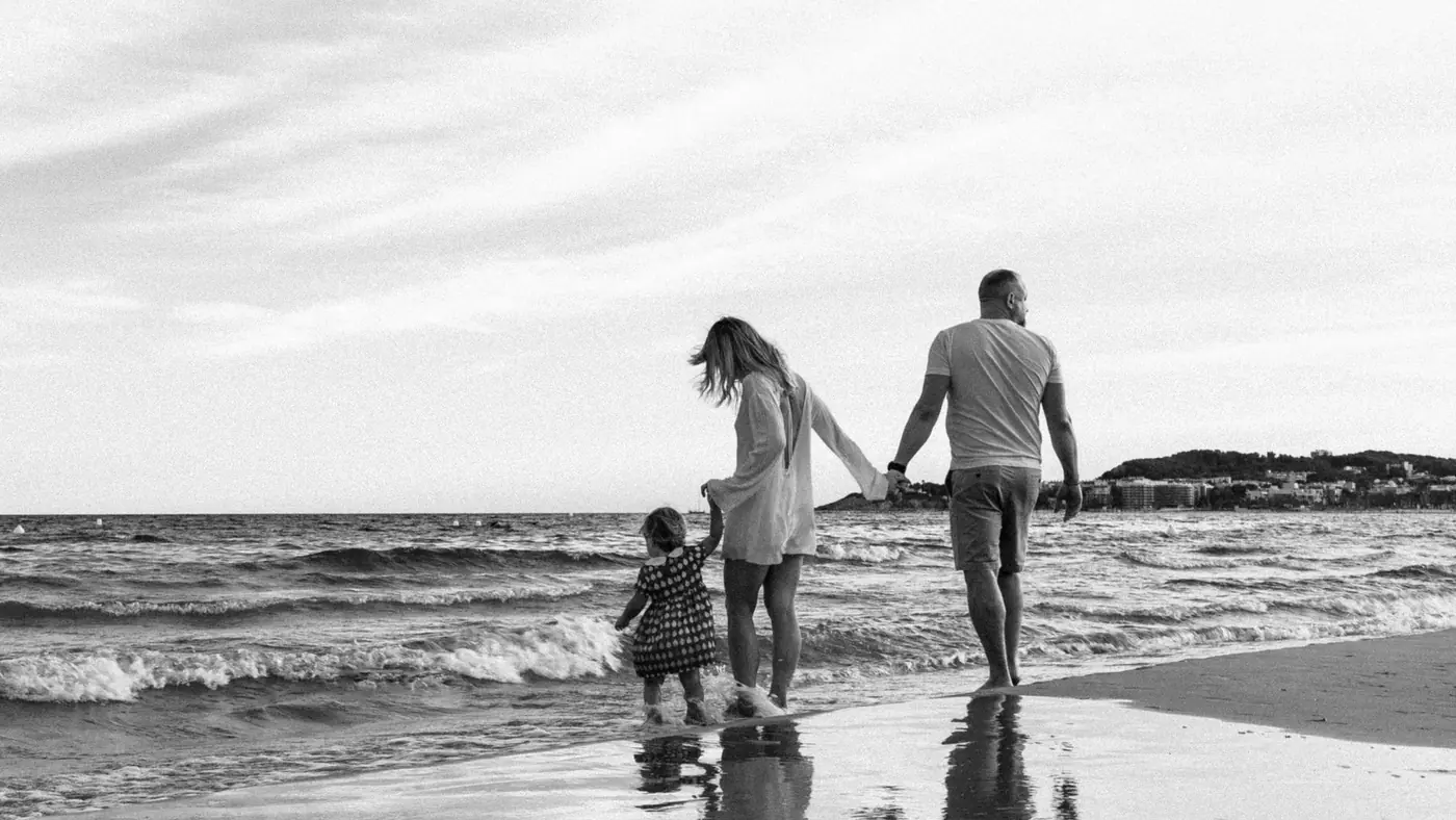 A family enjoys a peaceful walk along the beach with gentle waves.