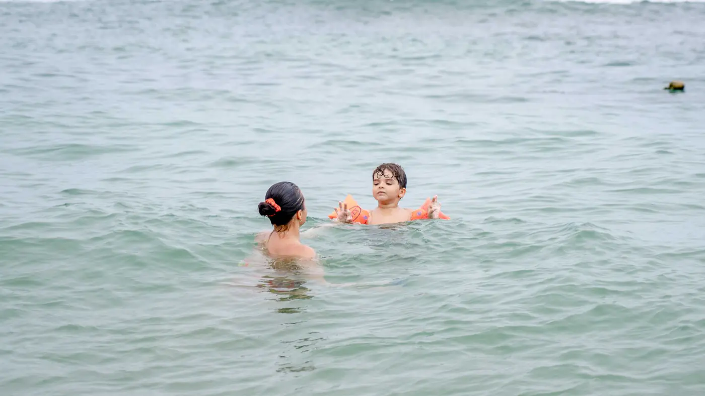 A mother and her child swim in the ocean, enjoying a relaxing day at the beach.