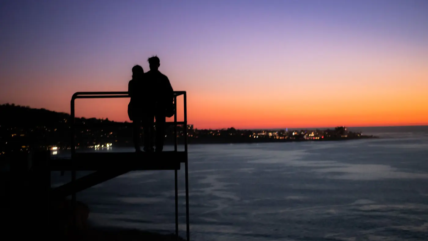 Silhouette of a romantic couple on a watch tower against stunning ocean sunset.
