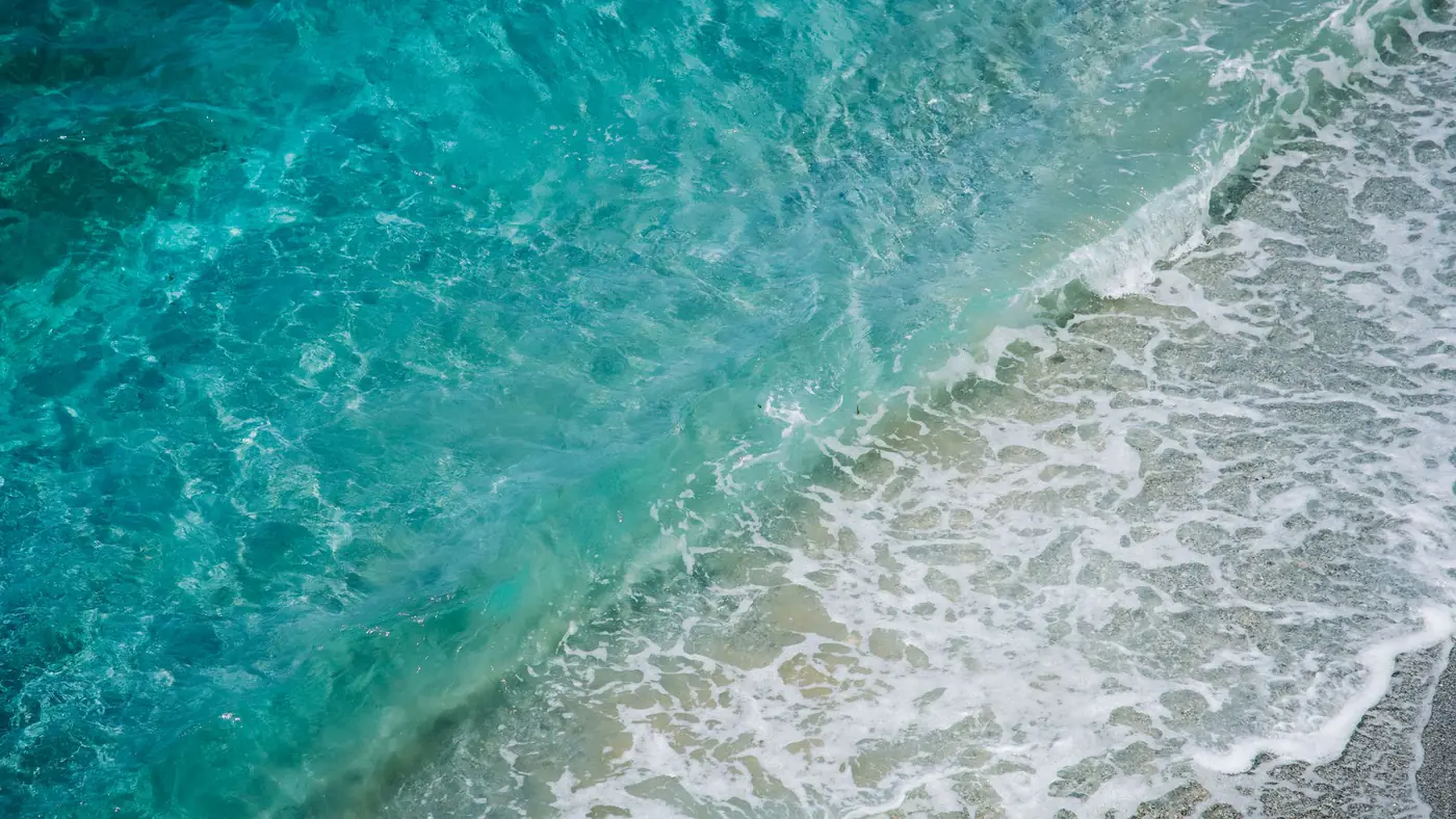 Vibrant aerial view of turquoise ocean waves crashing onto a sandy shore, showcasing the beauty of nature.