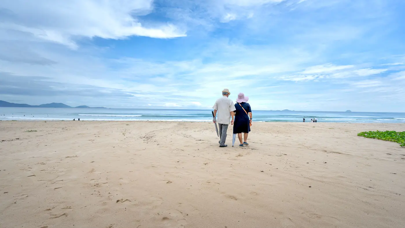 A senior couple walking on a serene sandy beach under a beautiful cloudy sky.