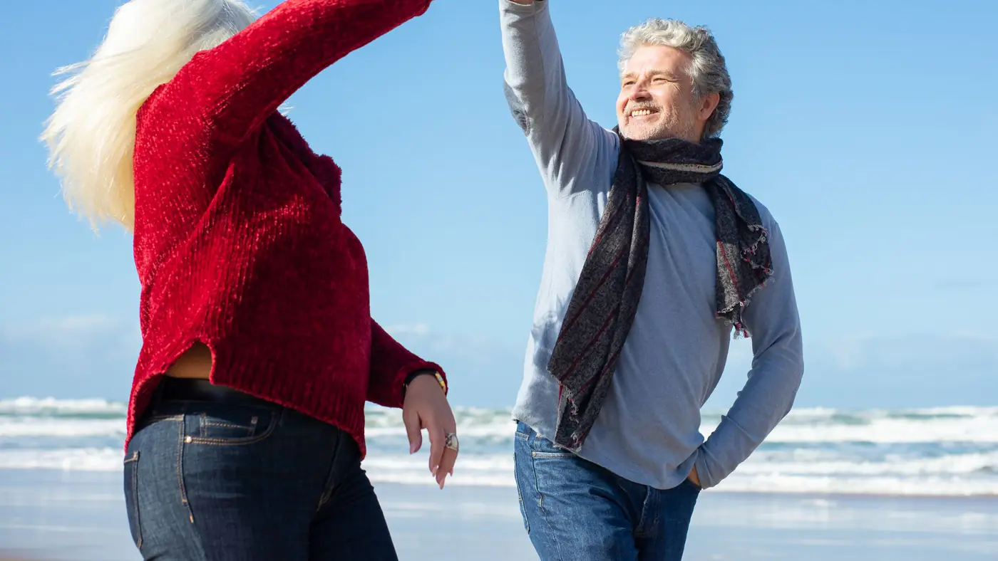 Elderly couple enjoying a dance on a sunny beach, showcasing love and happiness.