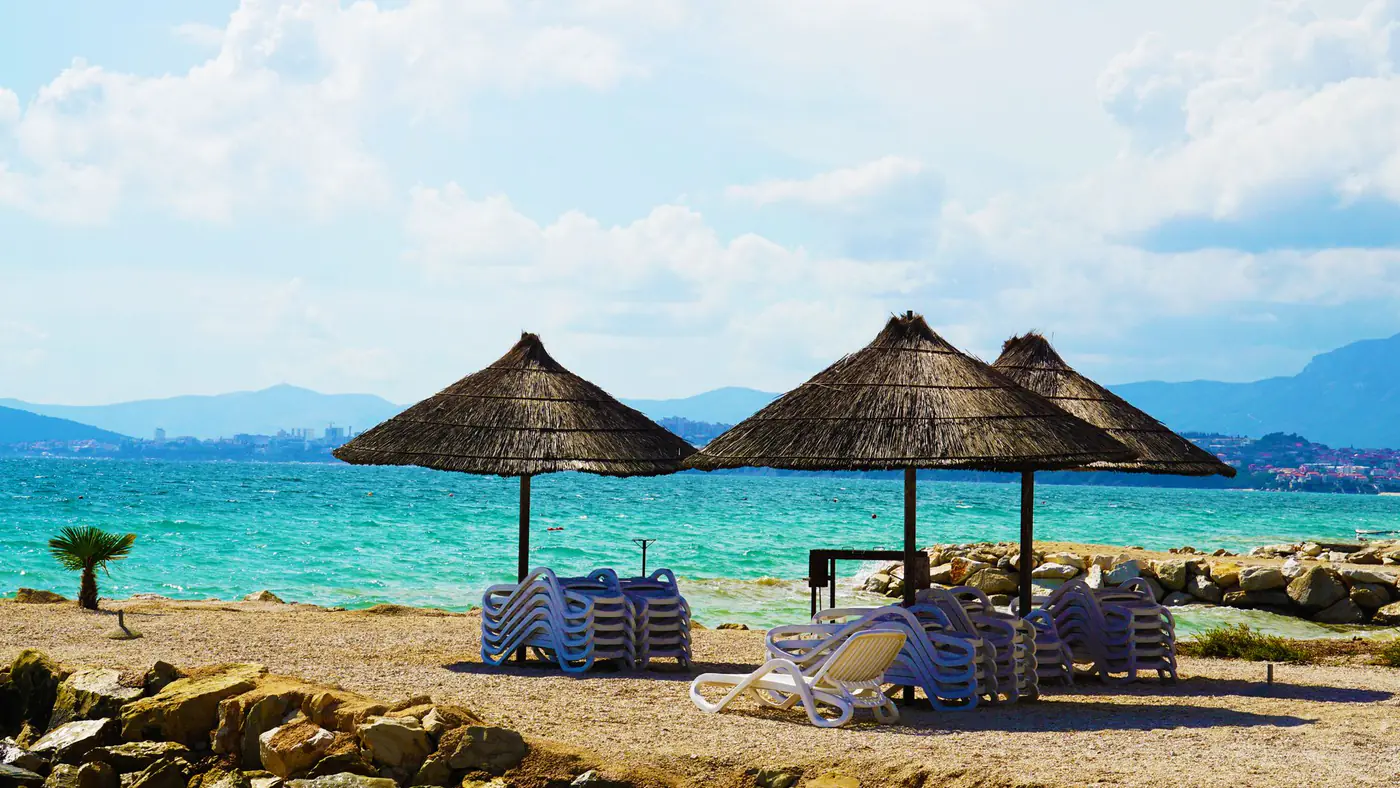 A serene beach scene with thatched huts, clear turquoise waters, and a tranquil summer sky.